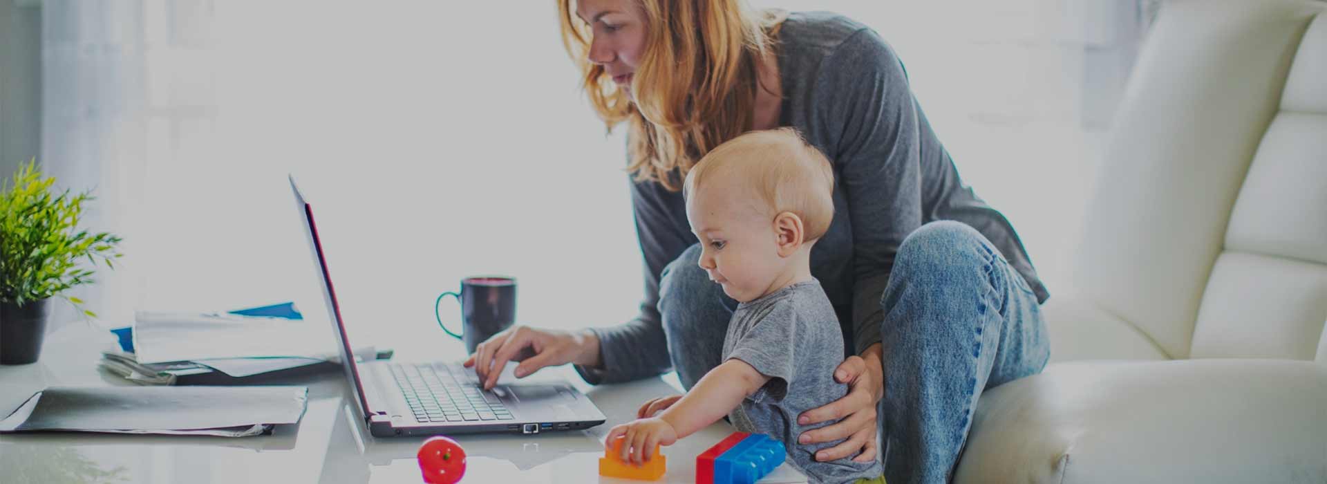Parent working on a laptop at home with a toddler